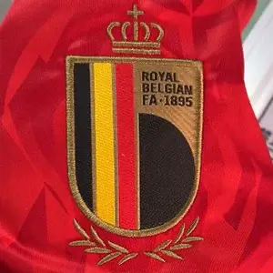 Royal Belgian FA national team crest on red fabric using professional Custom Soccer Jersey Embroidery.
