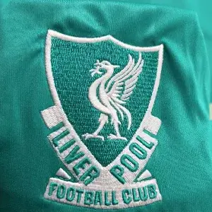 Intricate Liverpool FC Liver Bird crest on teal fabric through premium Custom Soccer Jersey Embroidery.